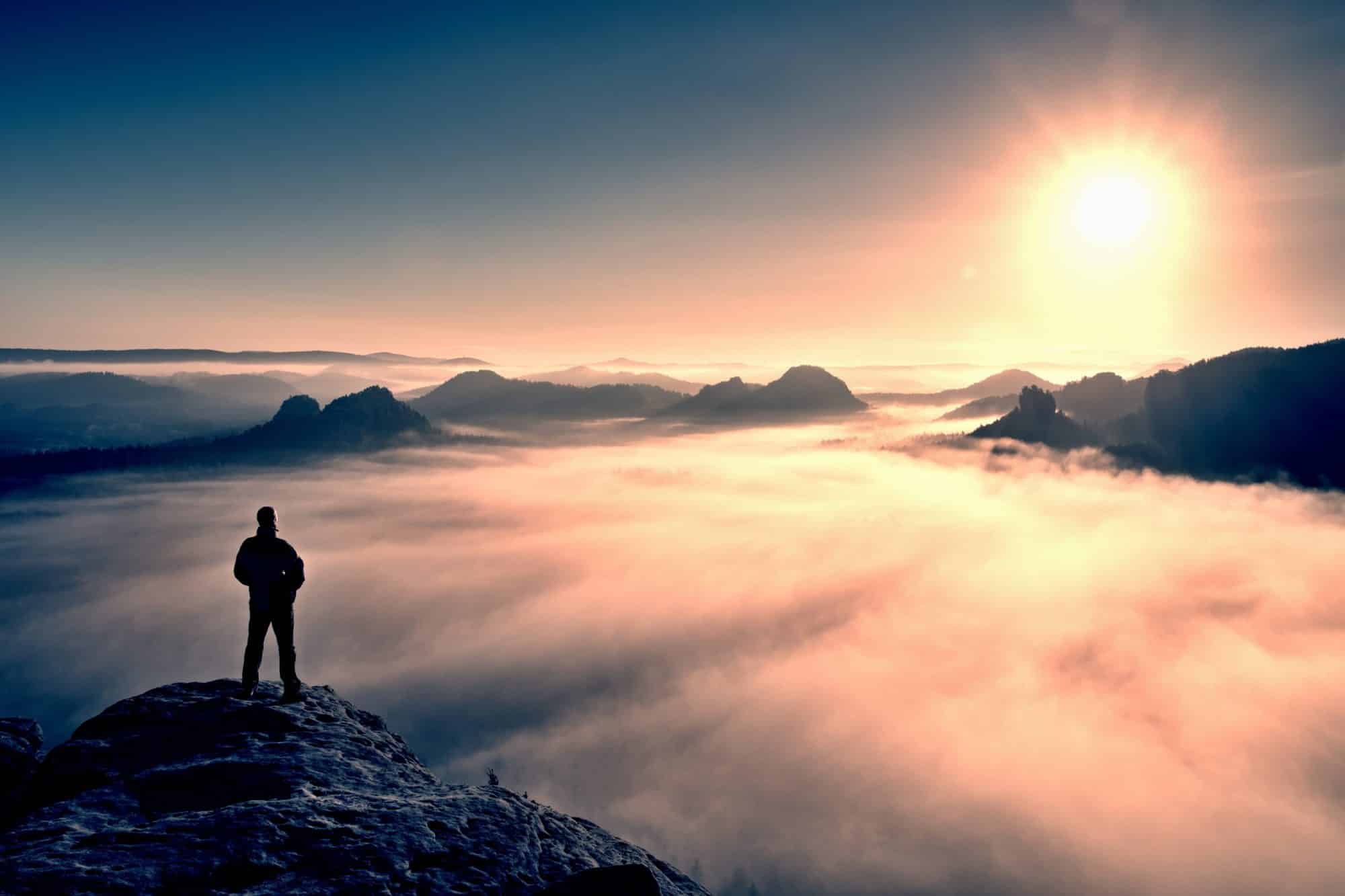 A man standing on a mountain looking at fog cover.