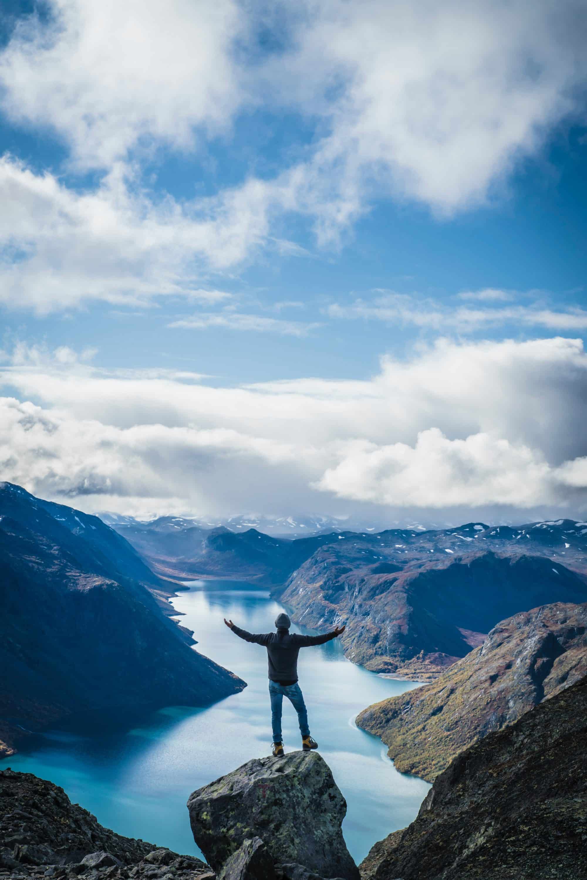 A man standing on a mountain overlooking water.
