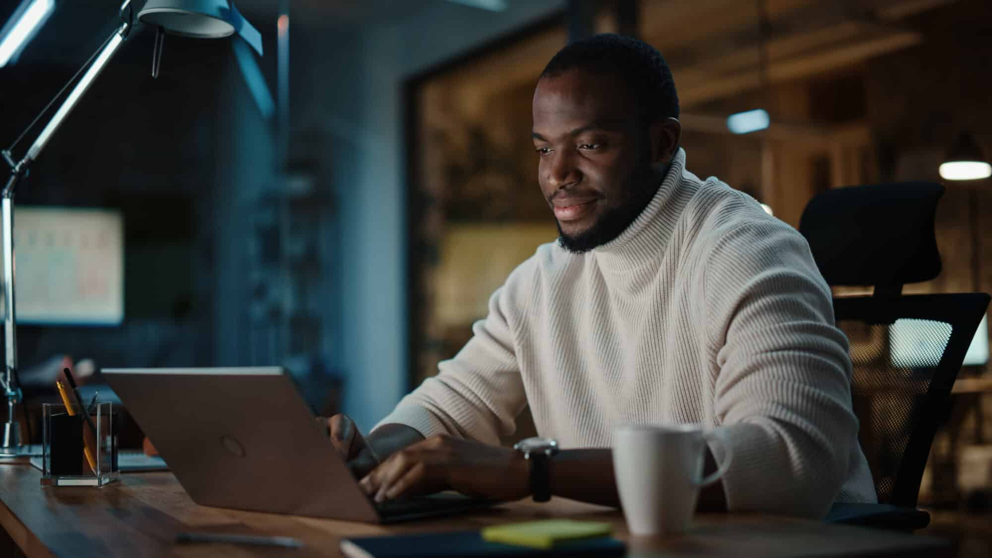 A man looking at a computer wearing a light sweater.