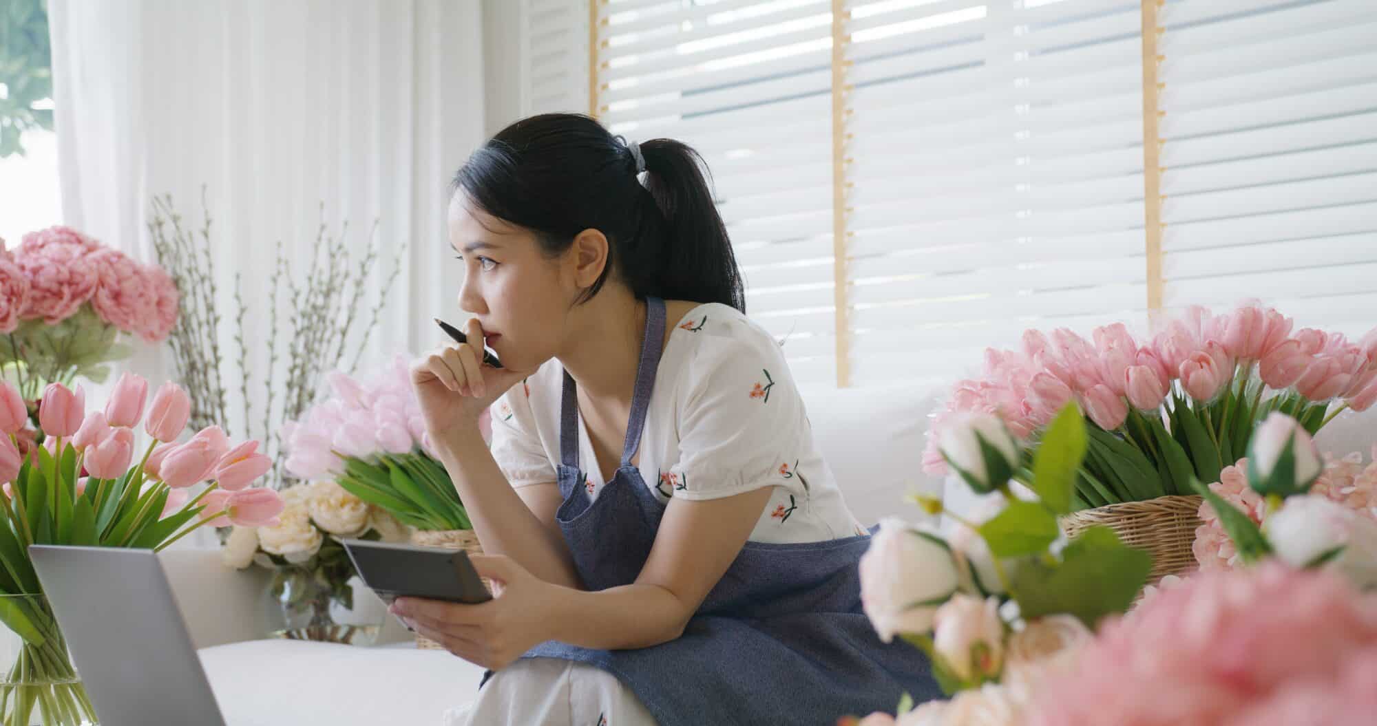 A woman sitting between flowers in a frustrated pose.