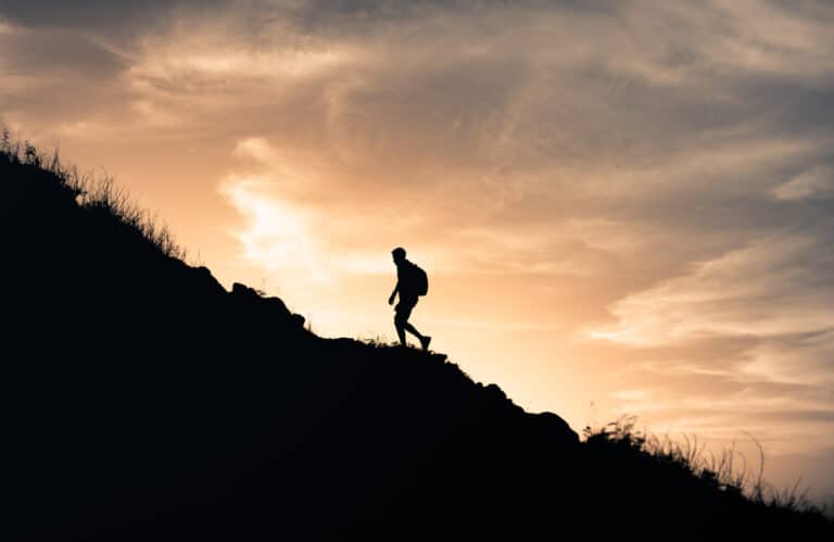 a person walking up a mountain with sunset in the background